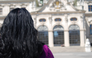 Frau mit langen, schwarzen Haaren sieht auf die großen Türen des Schlosses Belvedere – Jahresrückblick 2021. Sie tanzten um mein Leben